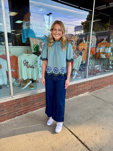 Solid short flutter sleeve top featuring floral embroidery and scallop hem.